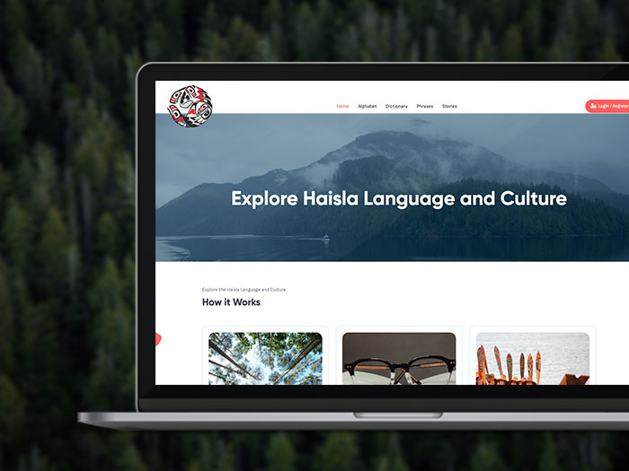 A laptop displaying a website focused on Haisla language and culture. The homepage features a navigation menu, an image of misty mountains and water, and sections titled "How it Works" with images below. The laptop background is a dense forest.